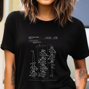 May include: A black short-sleeved t-shirt featuring a white graphic print of a United States Patent illustration for a rowing shell. The design includes technical line drawings of the boat, patent number 5,474,000, and the text United States Patent.
