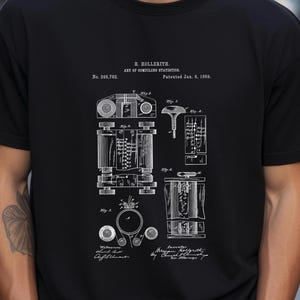 Puede incluir: Una camiseta negra con un estampado gráfico blanco del diseño de patente de H. Hollerith para el arte de compilar estadísticas, fechado el 8 de enero de 1889. El diseño incluye dibujos técnicos etiquetados de la Fig. 1 a la Fig. 6.