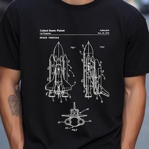 May include: A black t-shirt featuring a white graphic print of a United States Patent for a space vehicle, patent number 3,866,863, dated Feb. 18, 1975. The design includes three technical line drawings labeled Fig. 1, Fig. 2, and Fig. 3.