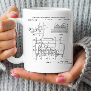 Könnte beinhalten: Eine weiße Keramiktasse mit einer Schwarzweißillustration eines Patents für einen Miniatur-Halbleiter-Integrierten Schaltkreis. Das Patent ist vom 24. Dezember 1963 und trägt den Titel "Miniatur-Halbleiter-Integrierter Schaltkreis". Das Patent ist von J.S. Kilby und die Patentnummer ist 3,115,581.