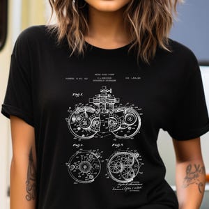 May include: A black short-sleeved t-shirt featuring a white graphic print of a United States patent illustration for an optometric instrument. The design includes technical line drawings labelled Fig 1, Fig 2, and Fig 3 with patent text details.