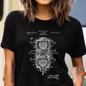 May include: A black t-shirt featuring a white graphic print of a United States patent illustration for a traffic signal by W.J. Leppert. The design includes technical line drawings, labels, and patent text details centered on the front of the shirt.