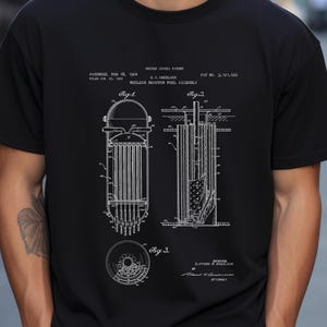 Puede incluir: Camiseta negra con un esquema blanco de un conjunto de combustible de reactor nuclear. El diseño incluye diagramas etiquetados como Fig. 1, Fig. 2 y Fig. 3, junto con información de patente y el texto "NUCLEAR REACTOR FUEL ASSEMBLY."