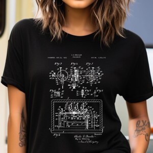 May include: A black short-sleeved t-shirt featuring a white screen-printed technical patent illustration. The graphic displays detailed mechanical diagrams labeled Fig. 2 through Fig. 8, including text reading C.R. DRECKLER POLYGRAPH, PAT. NO. 1,972,036.