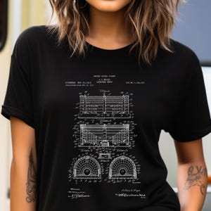 Könnte beinhalten: Ein schwarzes T-Shirt mit einem weißen Grafikdruck eines US-Patents für eine Hummerfalle. Das Design enthält technische Strichzeichnungen, Diagramme und den Patenttext, einschließlich des Titels Lobster Trap und der Patentnummer 1.070.195.