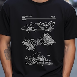 Puede incluir: Camiseta negra con un esquema blanco de patente de bobsleigh. El diseño incluye diagramas etiquetados FIG.1, FIG.2 y FIG.6, y texto que indica "United States Patent" y detalles de la patente.