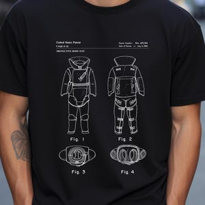 May include: A black t-shirt with a white graphic of a patent design for a protective body suit. The design includes four figures showing different views of the suit. The text on the shirt reads "United States Patent", "Crupi et al.", "Protective Body Suit", "Patent Number: Des. 429,354", "Date of Patent: Aug. 8, 2000", "Fig. 1", "Fig. 2", "Fig. 3", and "Fig. 4".