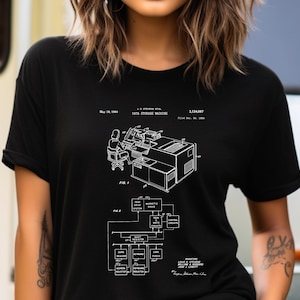 May include: A black short-sleeved t-shirt featuring a white technical patent illustration of a data storage machine. The graphic includes detailed schematics, labels such as 'Data Storage Machine', 'Fig. 1', 'Fig. 2', and inventor names printed in white.