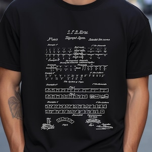 May include: A black t-shirt featuring a white graphic print of the S. F. B. Morse Telegraph Signs patent illustration. The design displays detailed technical diagrams, various telegraphic codes, and historical text from the 1840 patent document.