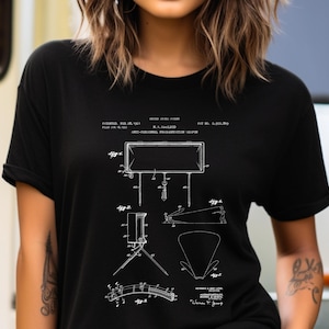 Może przedstawiać: Czarny t-shirt z krótkim rękawem z białą ilustracją techniczną patentu. Grafika przedstawia kilka widoków broni odłamkowej przeciwpiechotnej, w tym oznaczone figury, linie techniczne oraz szczegóły tekstu patentowego nadrukowane z przodu.