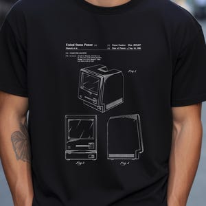 May include: A black t-shirt featuring a white graphic print of a United States Patent for a computer housing, patent number Des. 285,687, dated September 16, 1986. The design includes three technical line drawings labeled Fig. 1, Fig. 2, and Fig. 4.