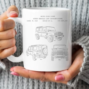 Puede incluir: Taza de cerámica blanca con una ilustración en blanco y negro de un diseño de patente de vehículo motorizado (SUV Station-Wagon). La taza incluye la fecha de la patente, 8 de marzo de 2022, y el número de patente D946,322.
