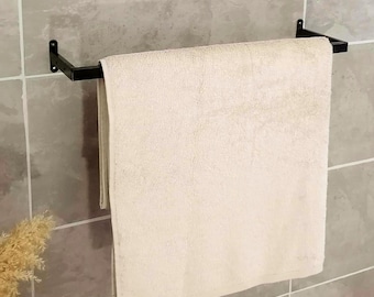 May include: A black metal towel rack mounted on a tiled wall, holding a folded, cream-colored towel. The wall tiles are a light gray with subtle veining. The towel is rectangular and appears soft.