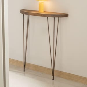 May include: A modern, half-moon console table with a dark wood top and slender, bronze-colored metal legs. A yellow table lamp sits on the table. The lamp has a cylindrical base and a rounded top. The table is 30 inches long.