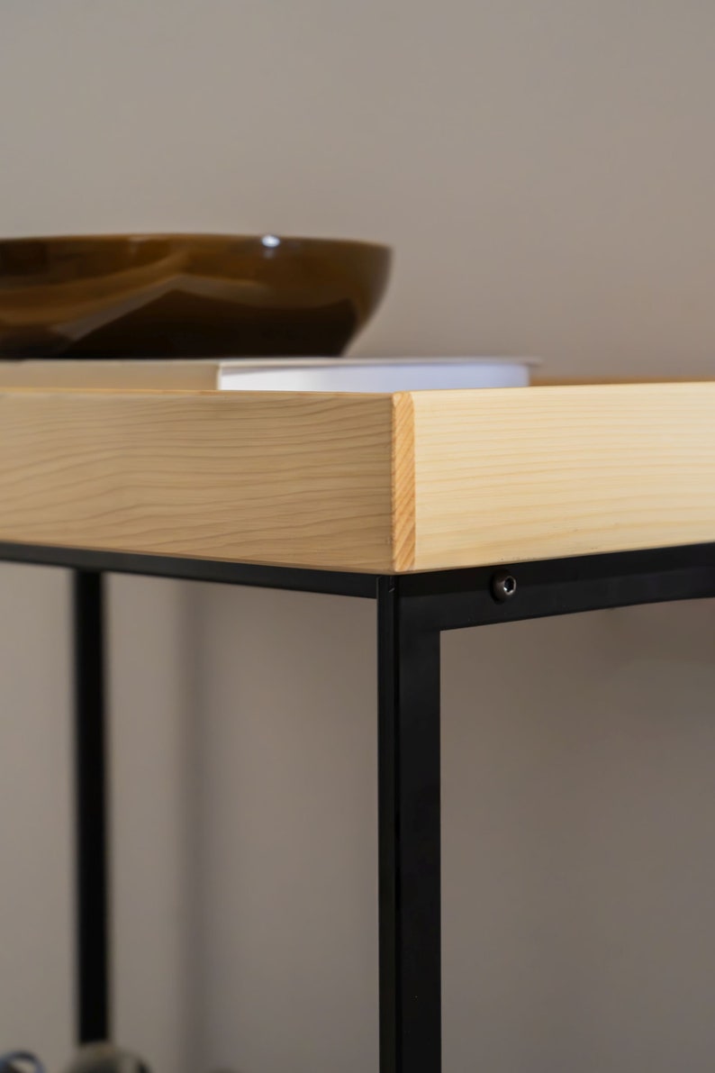 Pu&ograve; includere: Uno scaffale in legno con una struttura in metallo nero. Lo scaffale &egrave; in legno chiaro e ha una finitura naturale. La struttura in metallo &egrave; nera e ha un design semplice.