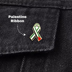 Può includere: Spilla a nastro Palestina con colori smaltati verde, bianco, nero e rosso. La spilla, a forma di nastro, è posta su uno sfondo di denim scuro. Il testo "Palestine Ribbon" è visibile.
