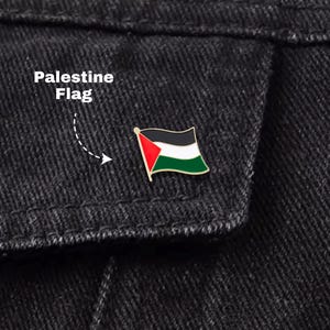 May include: A Palestine flag pin with red, white, black, and green colors is attached to a black denim jacket. The text "Palestine Flag" is written above the pin.