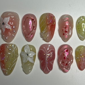 Puede incluir: Diez puntas de uñas rosas y amarillas con diferentes diseños, incluyendo flores, mariposas y purpurina.