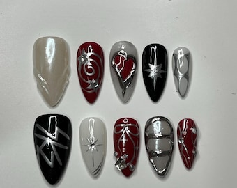 May include: A set of ten artificial nails in various designs. The nails feature a pearlescent, silver, red, and black color scheme. Designs include swirls, hearts, stars, and geometric patterns. Some nails have added embellishments.