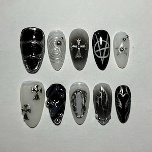 May include: Ten black and white press-on nails with various designs, including crosses, swirls, and hearts. The nails are decorated with silver studs and rhinestones.
