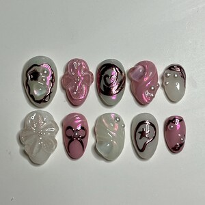 May include: Ten white and pink iridescent nail tips with various designs, including a star, a heart, a bow, and a flower.
