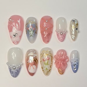 Puede incluir: Conjunto de diez uñas postizas con varios diseños. Las uñas son de forma almendrada y presentan detalles florales, de perlas y de cintas. Las uñas son en tonos de rosa, blanco y azul.