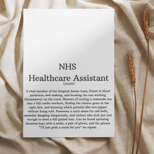 Puede incluir: Una impresión rectangular blanca con el texto "NHS Healthcare Assistant (sustantivo):" y una descripción detallada del rol. La impresión está sobre un fondo de tela beige con espigas de trigo secas.