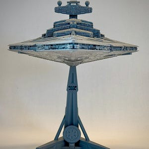 May include: A grey Star Destroyer model on a grey stand with a three-pronged base. The stand has a circular emblem with a symbol on it.