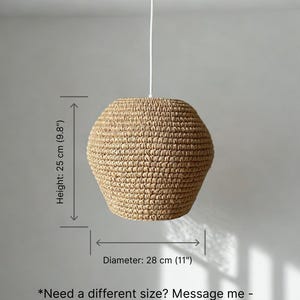 May include: A woven pendant light fixture with a natural, beige color. The lamp has a diameter of 11 inches and a height of 9.8 inches. It hangs from a white cord. The lamp's textured surface is visible.