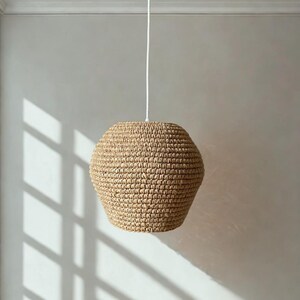 May include: A beige, woven pendant light fixture. The light has a rounded, geometric shape and is suspended from a white cord attached to a ceiling fixture. The light casts shadows on the wall.