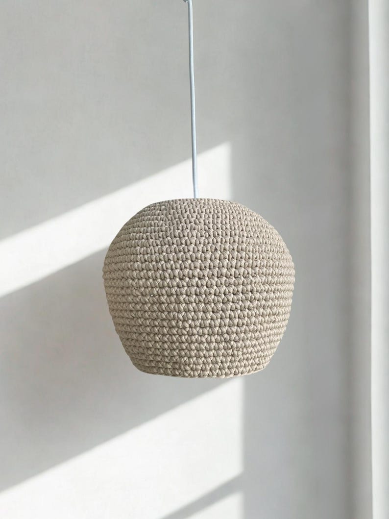 May include: A beige, spherical crochet pendant light fixture. The light hangs from a thin, light-colored cord. The shade has a textured surface and a rounded shape, suitable for home decor.