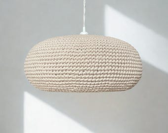 May include: A beige, round, crocheted pendant light fixture with a textured, knotted surface. The lamp is suspended from a white cord and features a central white mounting component at the top, creating a soft, rounded, and uniform shape.