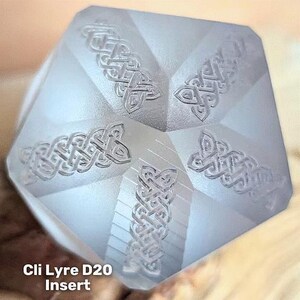 May include: A light gray, multi-faceted D20 die insert featuring intricate, raised Celtic knotwork patterns on each visible triangular face. The text 'Cli Lyre D20 Insert' is printed in white at the bottom left corner of the object.