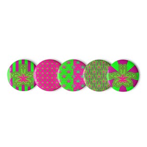 May include: Five circular pinback buttons featuring vibrant magenta and lime green patterns. The designs include vertical stripes, small repeating star shapes, a split color block, a grid pattern, and a central stylized leaf graphic on a sunburst.