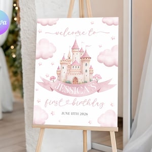 May include: A pink and white welcome sign on an easel. The sign features a watercolor illustration of a castle, clouds, and stars. Text includes "welcome to", "Jessica's first birthday", and the date June 15th 2026.