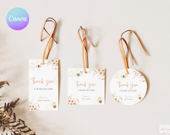 May include: Three thank you tags with a bee and floral design. The tags are white with gold lettering and are tied with brown twine. The text on the tags reads "Thank you for bee-ing here" and "[Name]'s Baby Shower".