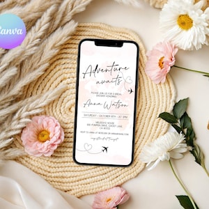 May include: A smartphone displays a bridal shower invitation with the text "Adventure awaits" and details for Anna Watson's shower. The phone rests on a woven mat, surrounded by flowers and decorative elements.