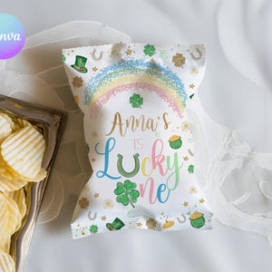 May include: A white chip bag with a rainbow, shamrocks, and the text "Anna's is Lucky One." The bag is decorated with gold accents and a green leprechaun hat. A silver tray of potato chips is in the background.