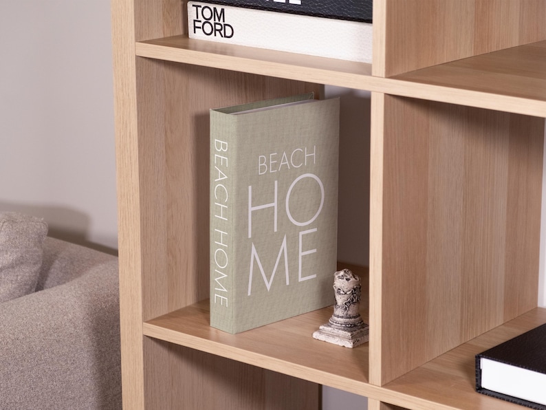 K&ouml;nnte beinhalten: Ein helles B&uuml;cherregal mit mehreren F&auml;chern. Ein Buch mit dem Titel "BEACH HOME" steht auf einem Regal. Eine kleine dekorative Statue und ein Buch mit dem Titel "TOM FORD" sind ebenfalls zu sehen.