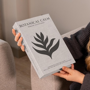 May include: A light grey book titled "BOTANICAL CALM" with a black leaf design. The book is part of the WORKART MASTER SERIES and has text that reads "INSPIRED BY LEAVES AND LIGHT. SOFT LINES THAT BREATHE LIFE INTO YOUR SPACE."