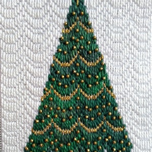 Op de afbeelding: Een groene kerstboom met gouden kralen en een gouden ster bovenop. De boom is geborduurd op een witte achtergrond.