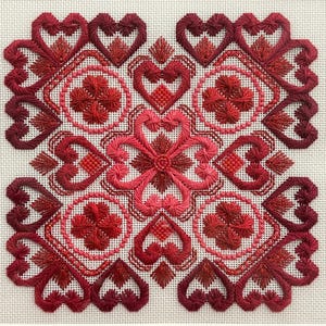 Könnte beinhalten: Ein rotes und weißes Stickmuster mit einem sich wiederholenden Muster aus Herzen und Blumen. Das Muster ist in verschiedenen Stichen gearbeitet, darunter Satinstich, französische Knoten und Samtstich.