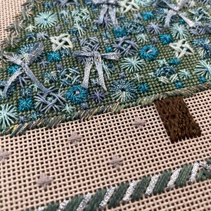 Peut inclure: Gros plan d'un sapin de No&euml;l brod&eacute; en vert et bleu avec un tronc en feutre brun. L'arbre est d&eacute;cor&eacute; de flocons de neige bleus et blancs et de n&oelig;uds.