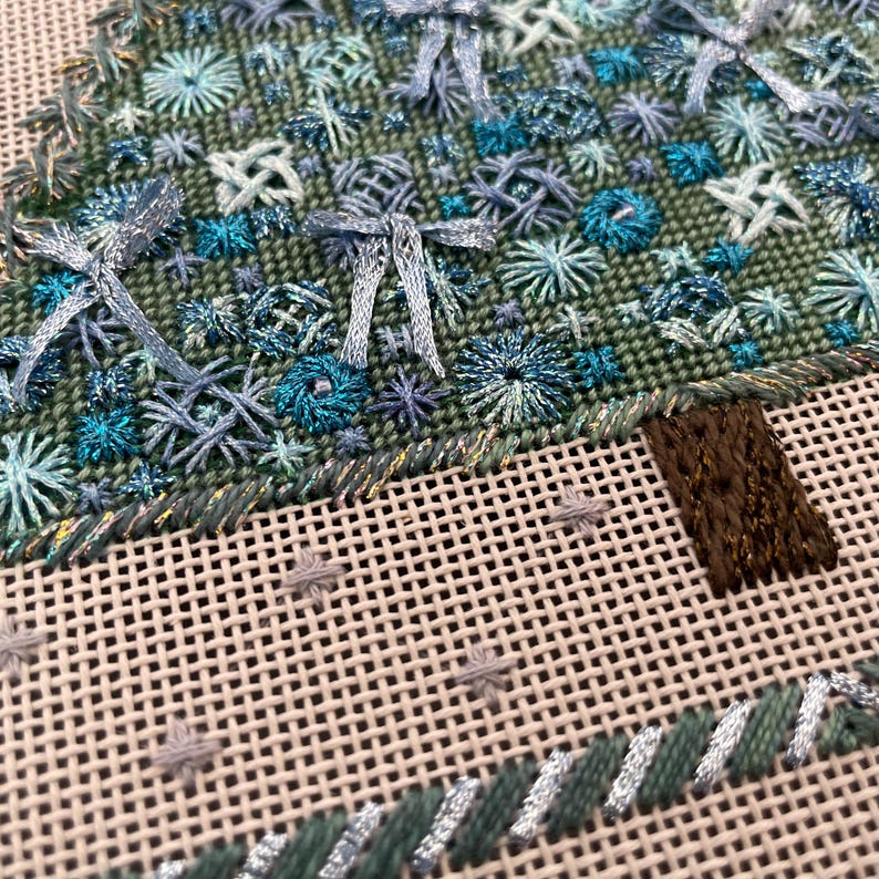 Peut inclure: Gros plan d'un sapin de No&euml;l brod&eacute; en vert et bleu avec un tronc en feutre brun. L'arbre est d&eacute;cor&eacute; de flocons de neige bleus et blancs et de n&oelig;uds.