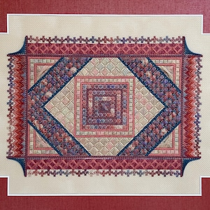 May include: An intricate needlepoint design with a central diamond and square pattern in red, blue, and beige. The detailed work includes a fringed border and is set against a neutral background, framed in a red mount.
