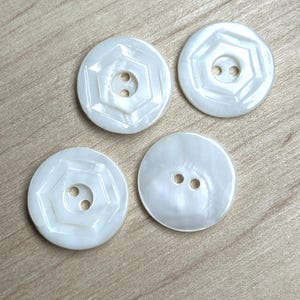 May include: Four white, round, plastic buttons with two holes each. Two of the buttons have a raised, geometric design.
