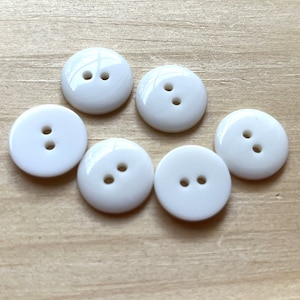 May include: Six white plastic buttons with two holes each. The buttons are round and have a smooth, glossy finish.