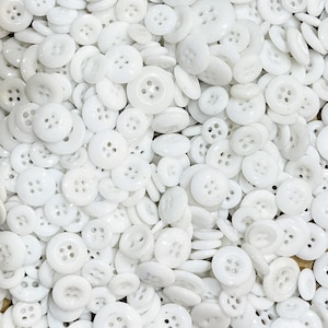 May include: A large collection of white plastic buttons of various sizes and shapes. The buttons have different numbers of holes, ranging from two to six.