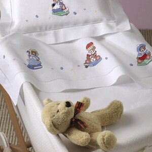 Puede incluir: Juego de ropa de cama para cuna blanca con osos de peluche bordados leyendo libros. El juego incluye una sábana bajera, una sábana plana y una funda de almohada. Un oso de peluche marrón está acostado en el colchón de la cuna.