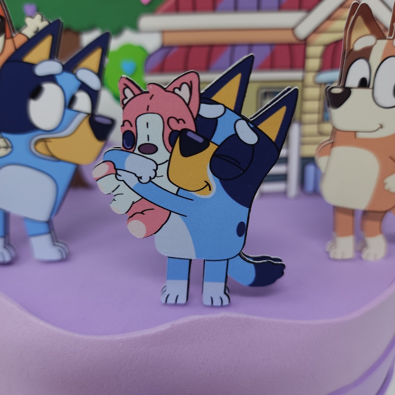 Puede incluir: Un perro de dibujos animados azul y blanco sosteniendo un perro de dibujos animados rosa. Los perros est&aacute;n de pie sobre un pastel morado.